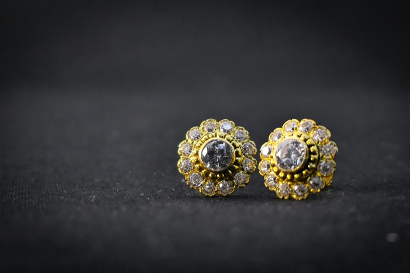 Gold and diamond stud earrings photographed on dark fabric