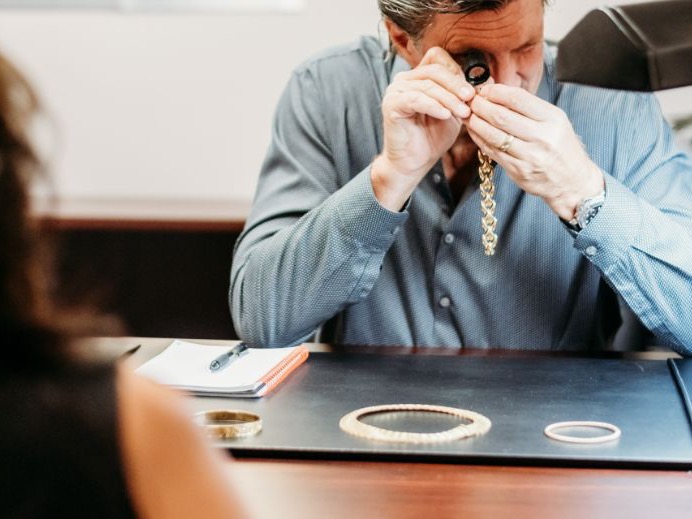 Jeweler examining a customer's gold chain through a loupe at the counter